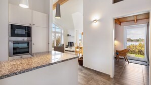 A modern kitchen with built-in appliances, a dining area with natural light, and a view through a glass door. - Holiday Home 'Sonnenuferhaus' with Sea View, Private Terrace and Wi-Fi (Kosel)