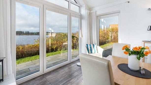 A modern room with large windows, a wooden table, and a vase of flowers. - Holiday Home 'Sonnenuferhaus' with Sea View, Private Terrace and Wi-Fi (Kosel)