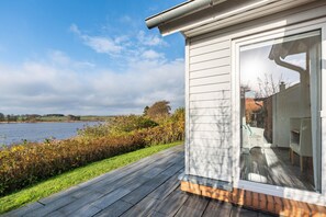 A modern house with a deck, a large window, and a view of a lake.