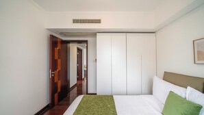 Une chambre d’hôtel avec un lit, un plaid vert, une tête de lit blanche et une armoire.