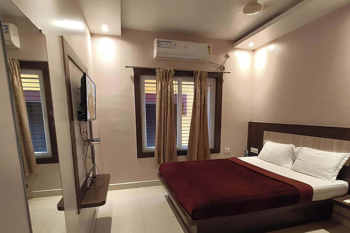 Una habitación de hotel moderna con una cama grande, un televisor de pantalla plana montado en la pared, un equipo de aire acondicionado y un ventilador de techo.