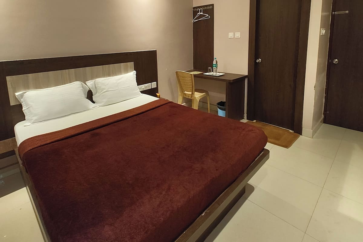 Una habitación de hotel con cama, escritorio, silla, armario y ventilador de techo.