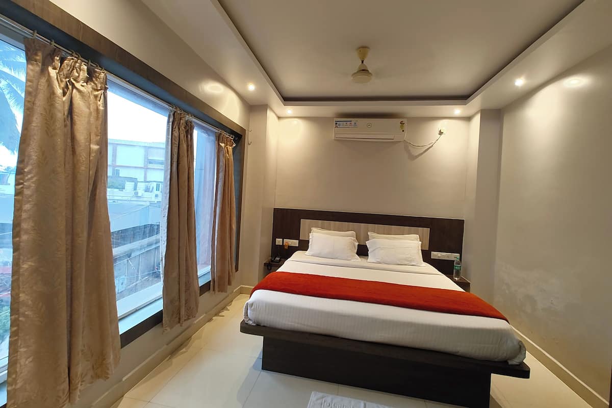 Una habitación de hotel moderna con cama, ventana con cortinas, equipo de aire acondicionado y ventilador de techo.