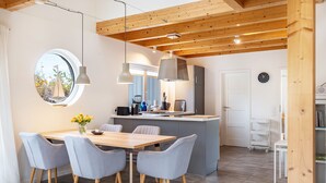 Une cuisine moderne avec un îlot central, un coin repas avec des chaises grises et une grande fenêtre donnant sur un voilier.