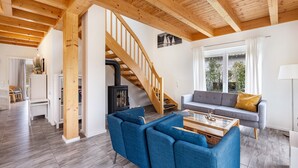 Un salon spacieux avec un escalier en bois, un canapé gris et un fauteuil bleu.