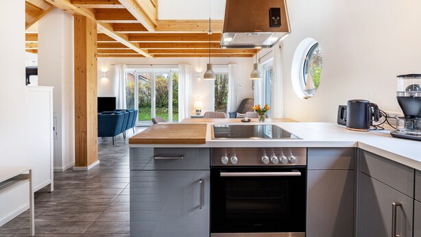 Une cuisine moderne dotée d’un îlot central, d’appareils électroménagers en acier inoxydable et d’un plafond en bois.