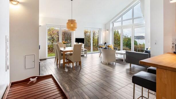 A spacious room with a dining area, a sofa, and large windows offering a view of the outdoors. - Holiday Home 'Schilfuferhaus' with Sea View, Private Terrace and Wi-Fi (Kosel)