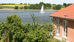 A house with a red roof, a sailboat on the water, and a green landscape in the background. - Holiday Home 'Schilfuferhaus' with Sea View, Private Terrace and Wi-Fi (Kosel)