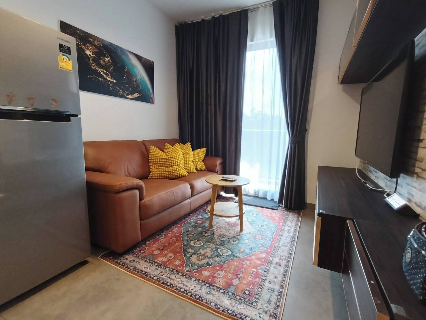 Un espace de vie compact comprenant un canapé, une petite table ronde, un téléviseur et un réfrigérateur.