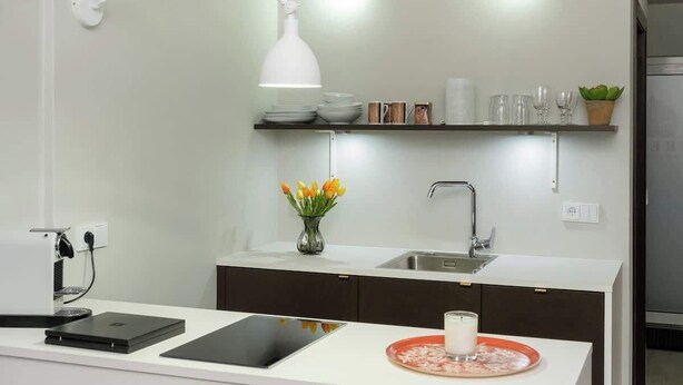 A modern kitchen with a white countertop, a built-in coffee machine, a tablet, a glass of milk, and a vase with flowers.