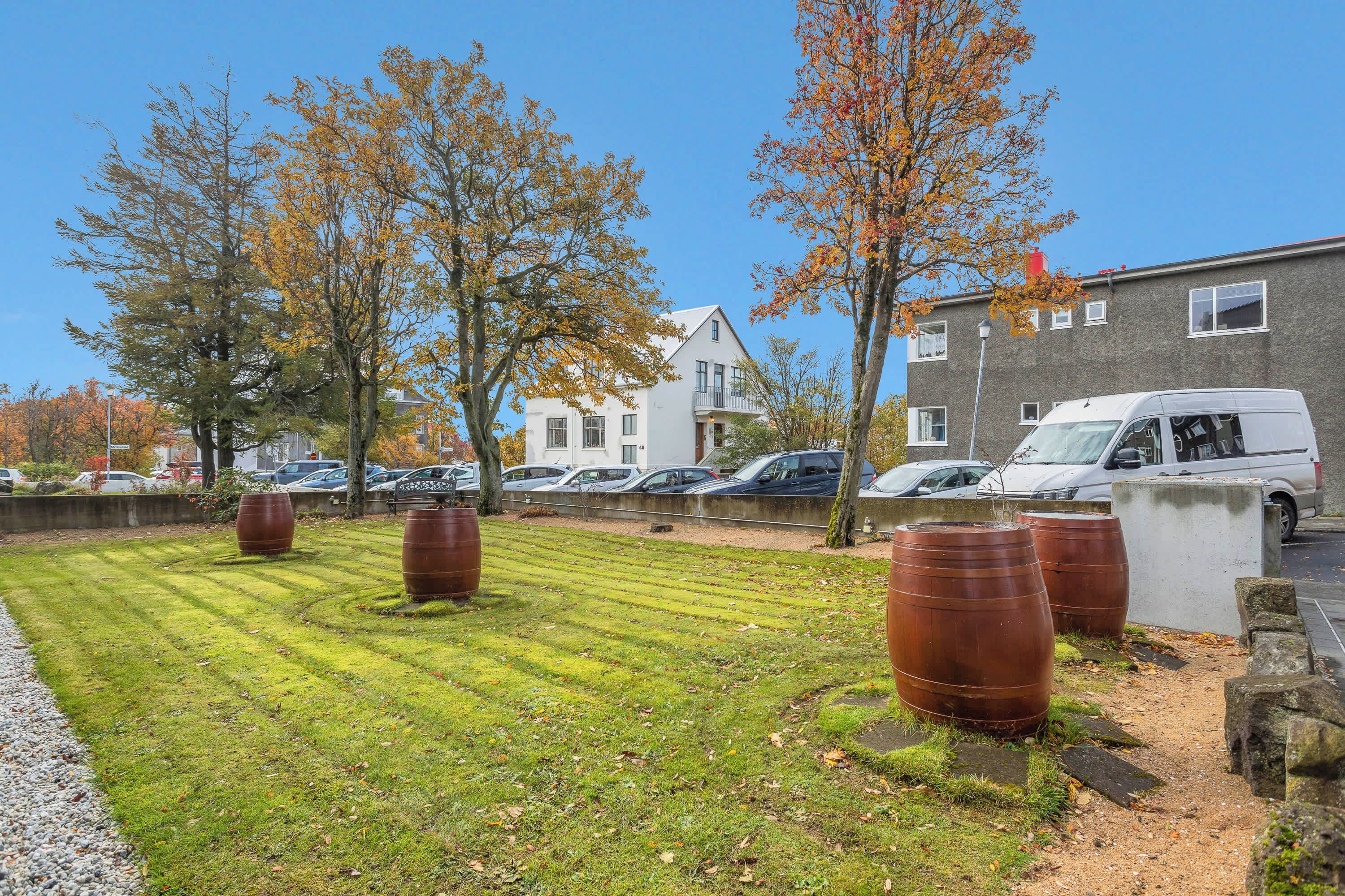 Een grasveld met grote metalen vaten, een wit gebouw en geparkeerde auto's op de achtergrond.
