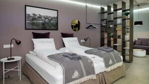 A modern bedroom with two beds, a large framed picture, a round mirror, and a built-in shelving unit.
