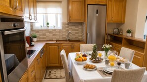 Une cuisine avec des meubles en bois, un réfrigérateur en acier inoxydable, une table à manger dressée pour le petit-déjeuner et une fenêtre ornée de plantes.