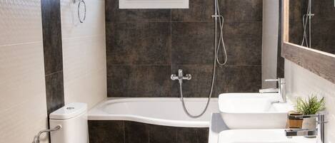 A modern bathroom with a bathtub, two sinks, a toilet, and a shower.
