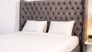 A bed with a tufted headboard, two pillows, and a bedside table with a plant.