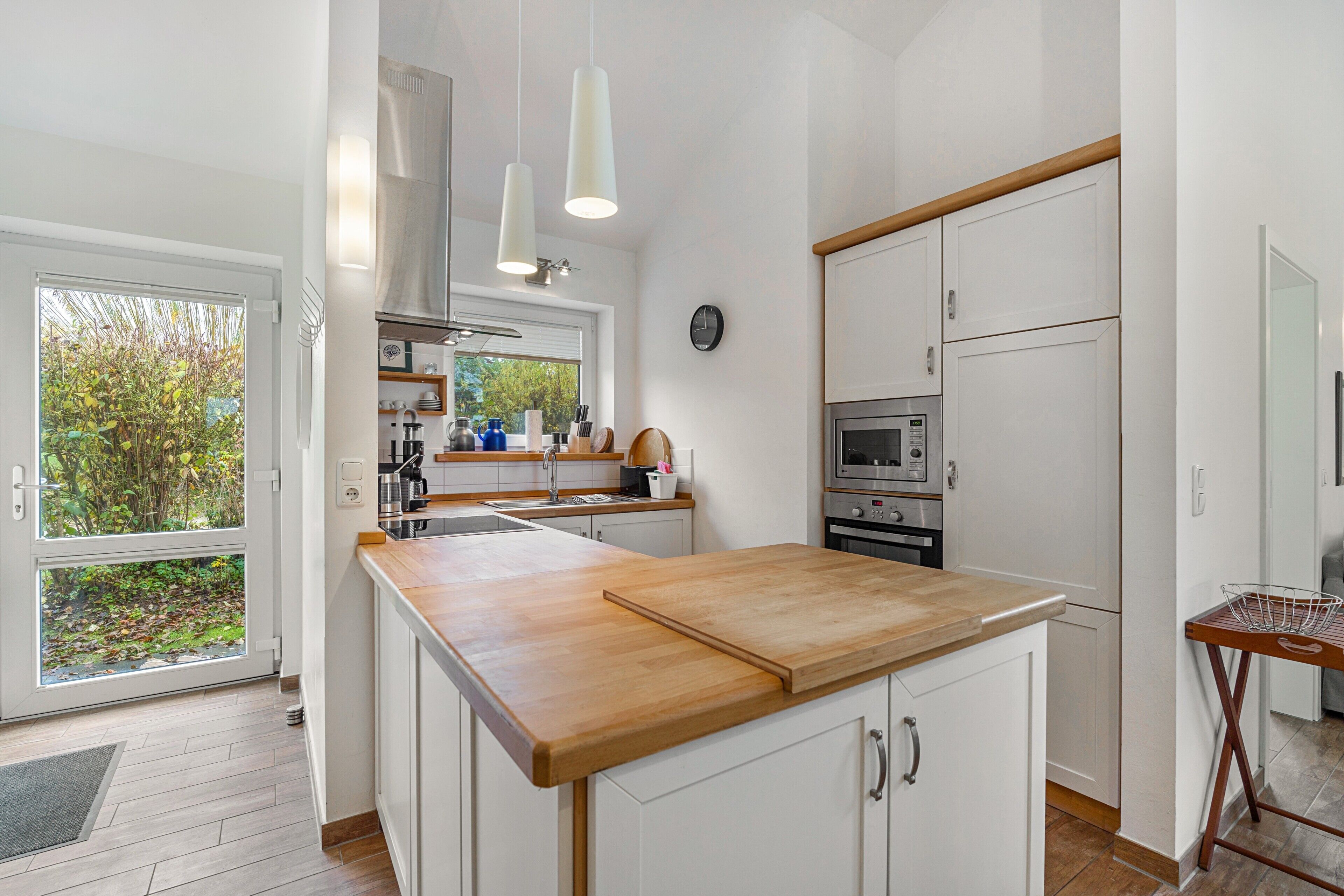 Una cucina moderna con piano di lavoro in legno, mobili bianchi, forno integrato e una finestra con vista sul verde.