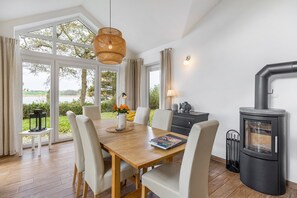 A dining area with a table, chairs, a hanging light, and a wood-burning stove. - Holiday Home 'Rosenuferhaus' with Sea View, Private Terrace and Wi-Fi (Kosel)