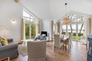 A spacious living area with a sofa, chairs, a dining table, and a TV. Large windows offer views of the outdoors. - Holiday Home 'Rosenuferhaus' with Sea View, Private Terrace and Wi-Fi (Kosel)