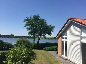 Une maison avec un toit rouge, un grand arbre et une vue sur un lac où l’on peut voir des voiliers.