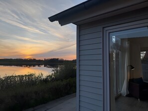 Une maison avec vue sur un coucher de soleil se reflétant sur une étendue d’eau, une porte-fenêtre coulissante et un espace patio.