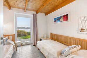 Une chambre avec deux lits, une fenêtre donnant sur un beau paysage, un plafond en bois et un tableau encadré au mur.