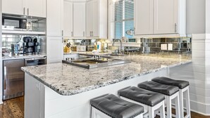 Una cocina moderna con armarios blancos, encimera de granito y una isla integrada con taburetes de bar.