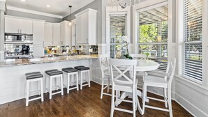 Una cocina moderna con armarios blancos, encimera de mármol y comedor con sillas blancas y una mesa redonda.