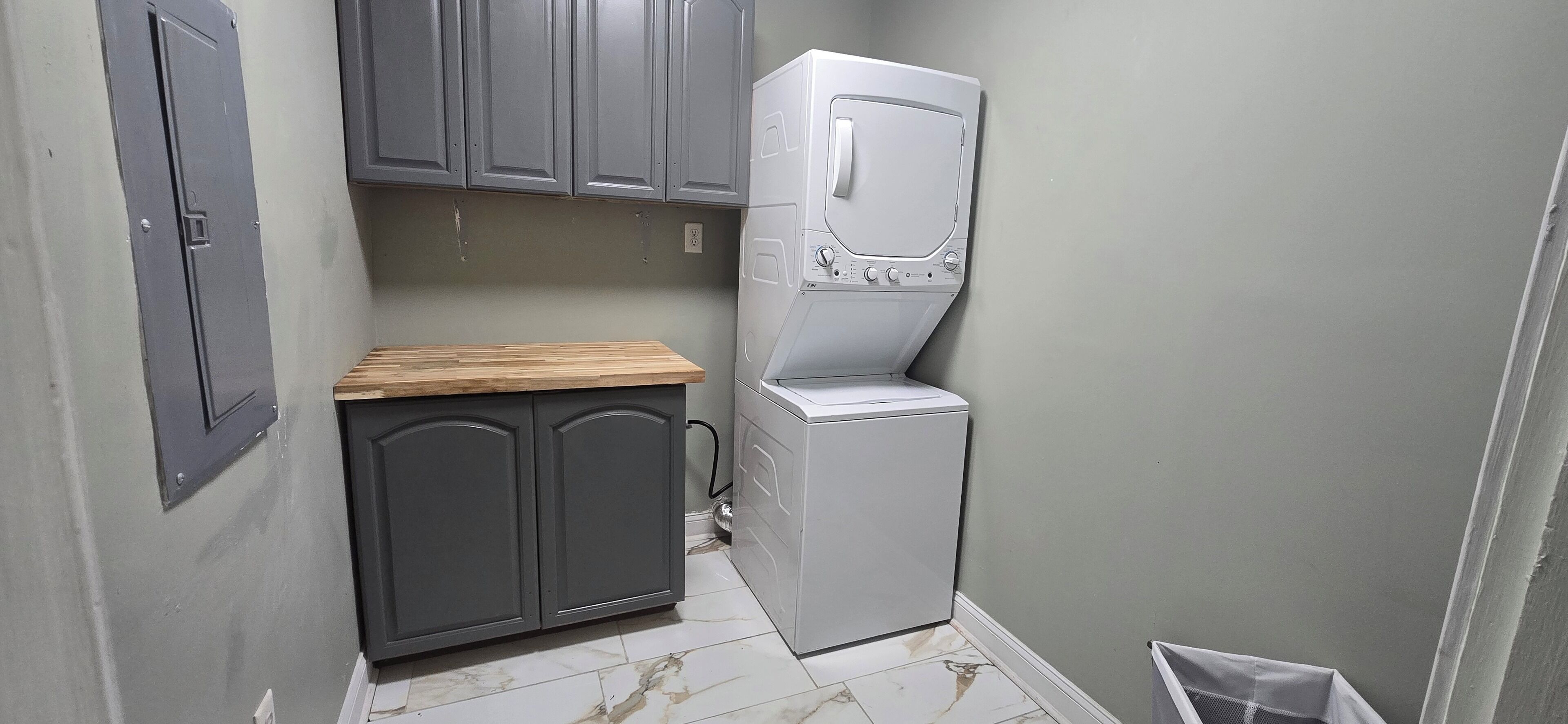 Une buanderie équipée d’un lave-linge et d’un sèche-linge, avec des armoires grises et un plan de travail en bois.