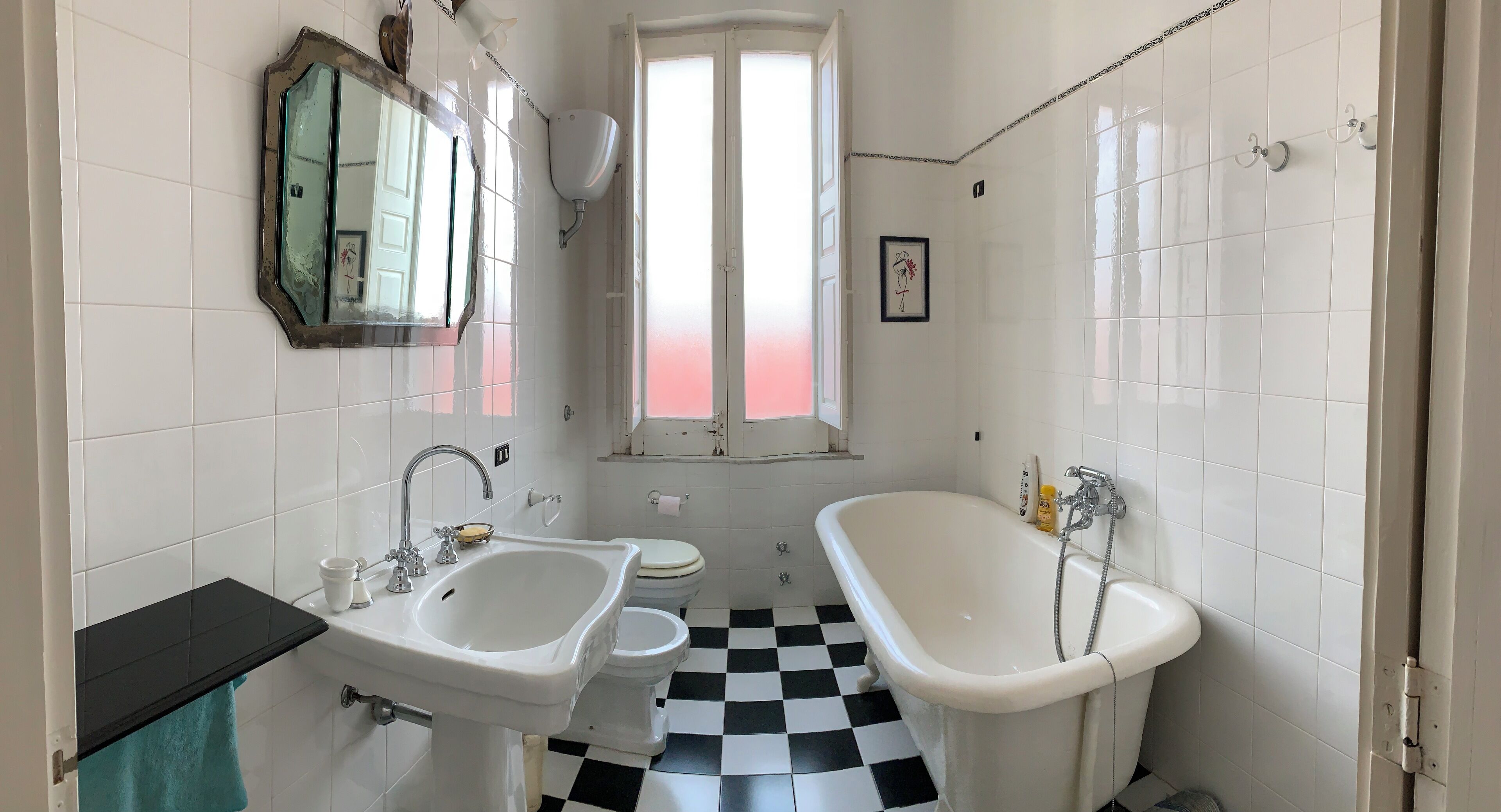 A bathroom with a black and white checkered floor, a white sink, a white toilet, a white bathtub, and a mirror with a decorative frame.
