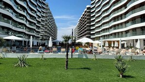 A modern hotel with a unique curved architecture, featuring multiple balconies and a central pool area with lounge chairs and umbrellas. - Casa del Mar 3 (Navodari)