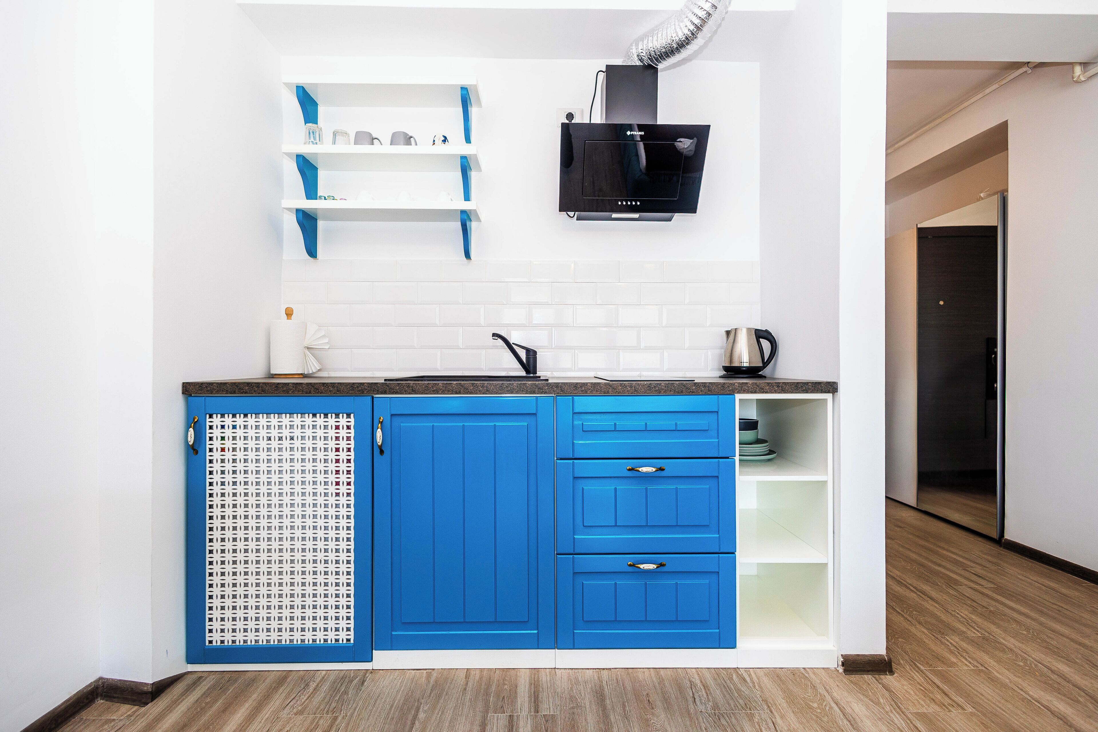 Een moderne keuken met blauwe kastjes, witte planken en een zwarte magnetron.