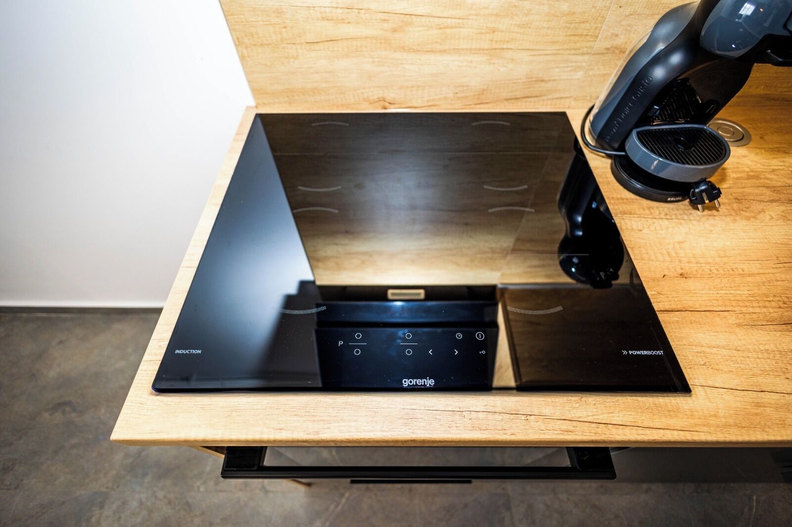 Een zwarte inductiekookplaat met een bedieningspaneel op een houten tafel.