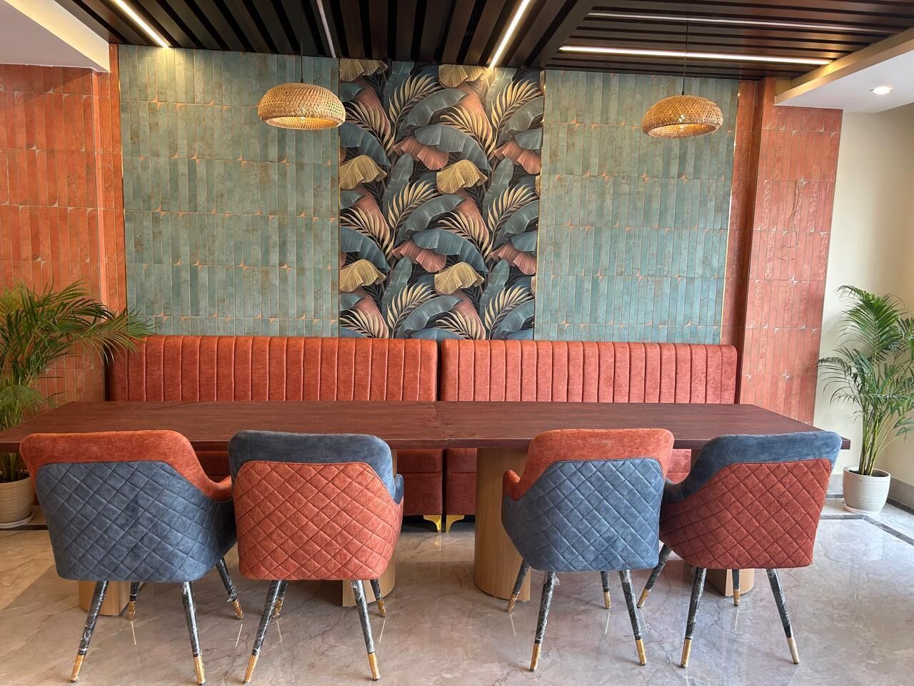 A dining area with a long wooden table, four chairs with quilted fabric, and a patterned wall behind the seating.