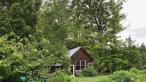 A rustic wooden cabin surrounded by lush greenery and a well-maintained garden. - Charming garden apartment with AC near Lake Fairlee, WFi. (Fairlee)
