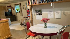 A room with a round table, red chairs, a bookshelf, a fire extinguisher, and a television. - Charming garden apartment with AC near Lake Fairlee, WFi. (Fairlee)