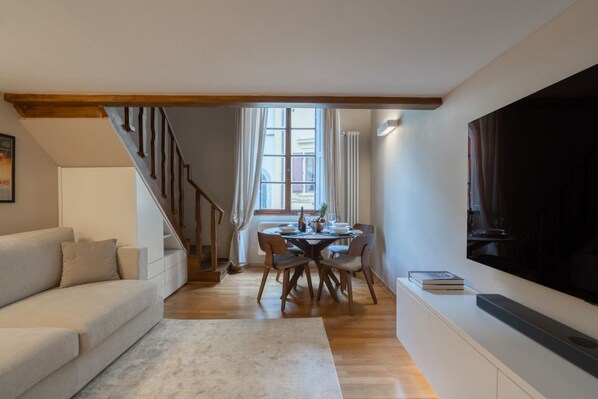 Un salon avec un canapé, une table à manger et des chaises, un escalier et un téléviseur fixé au mur.