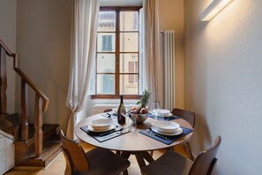 Un coin repas avec une table ronde, des chaises, un panier de fruits, des verres à vin et une bouteille.