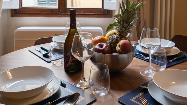 A dining table set with a bowl of fruit, wine glasses, and a bottle of wine. - Da Carlo Apartment in Pontevecchio (Firenze)