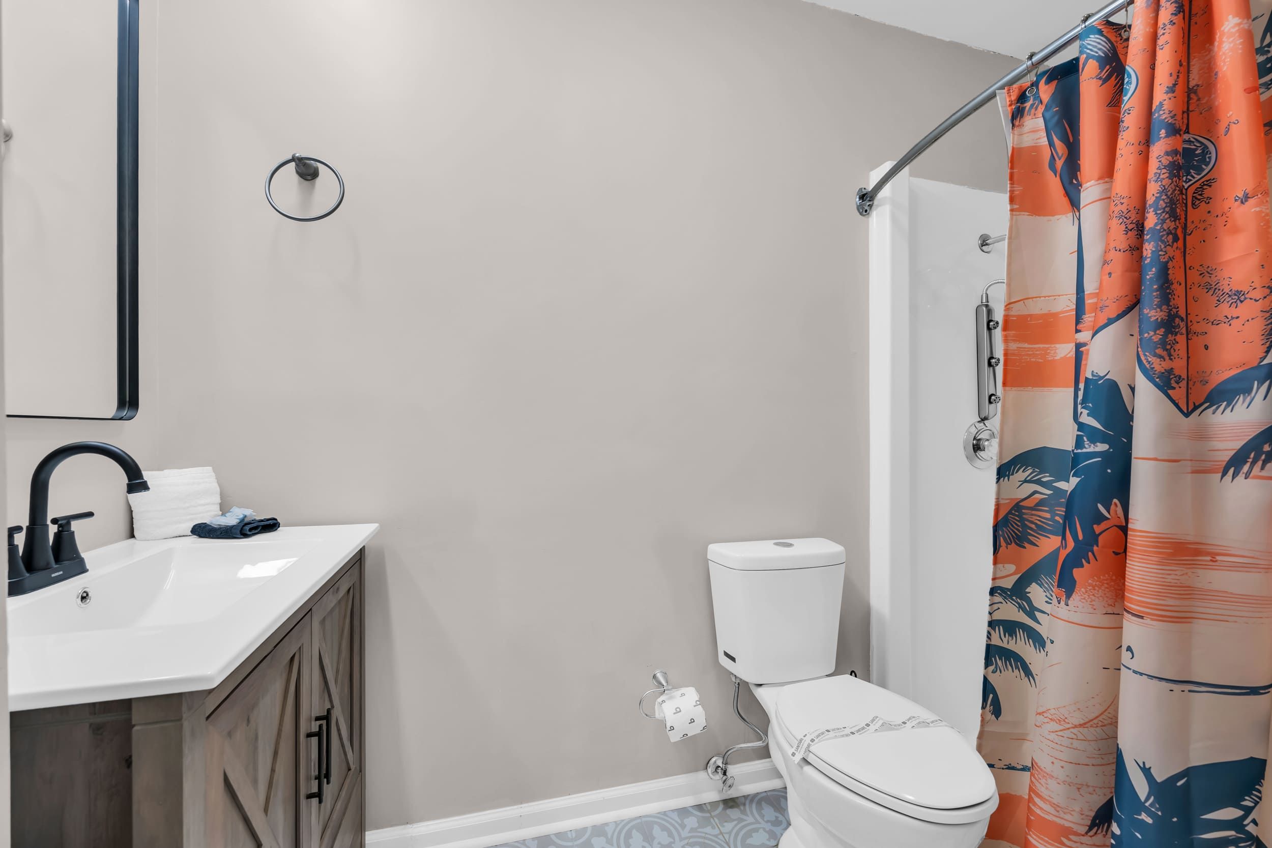 A bathroom with a white sink, dark wooden cabinets, a toilet, and a shower curtain with a tropical pattern.