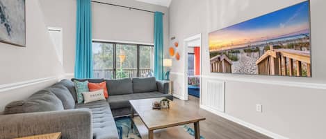 A modern living room with a sectional sofa, a coffee table, and a large painting of a beach scene.