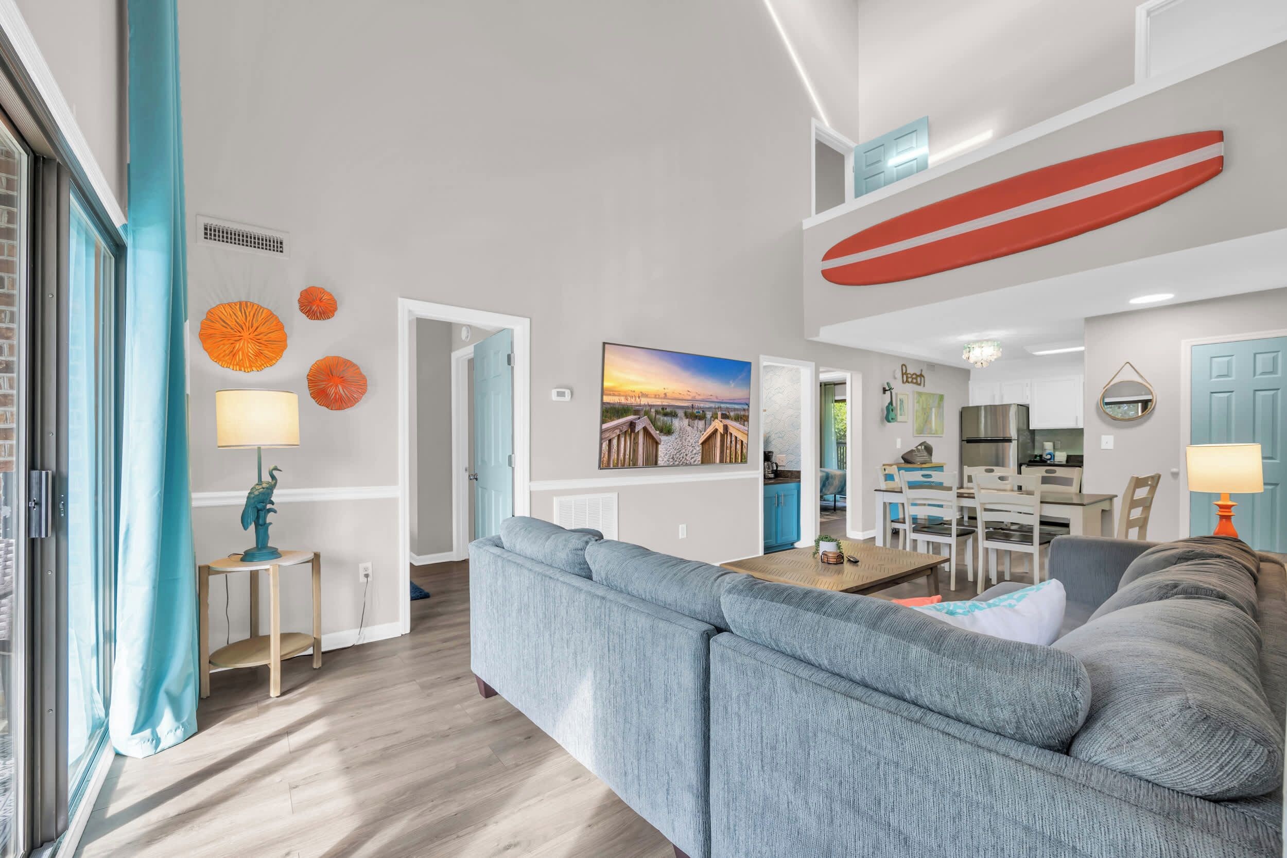 A modern living room with a grey sectional sofa, a dining area with a wooden table, and a kitchen in the background.