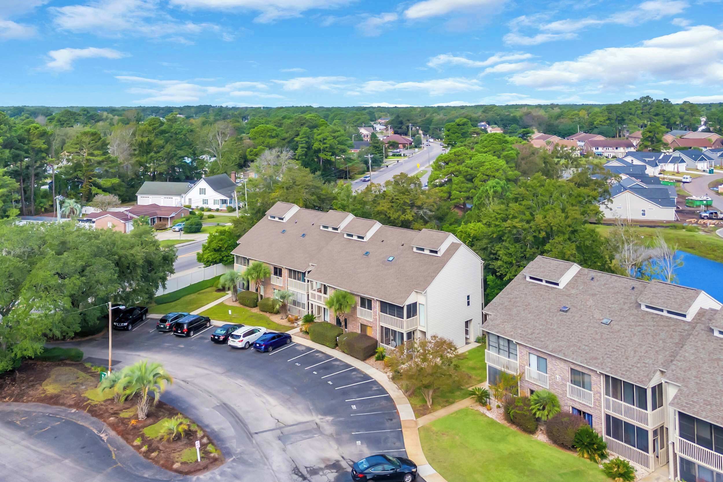 A residential area with a row of townhouses, a parking lot, and surrounding greenery.