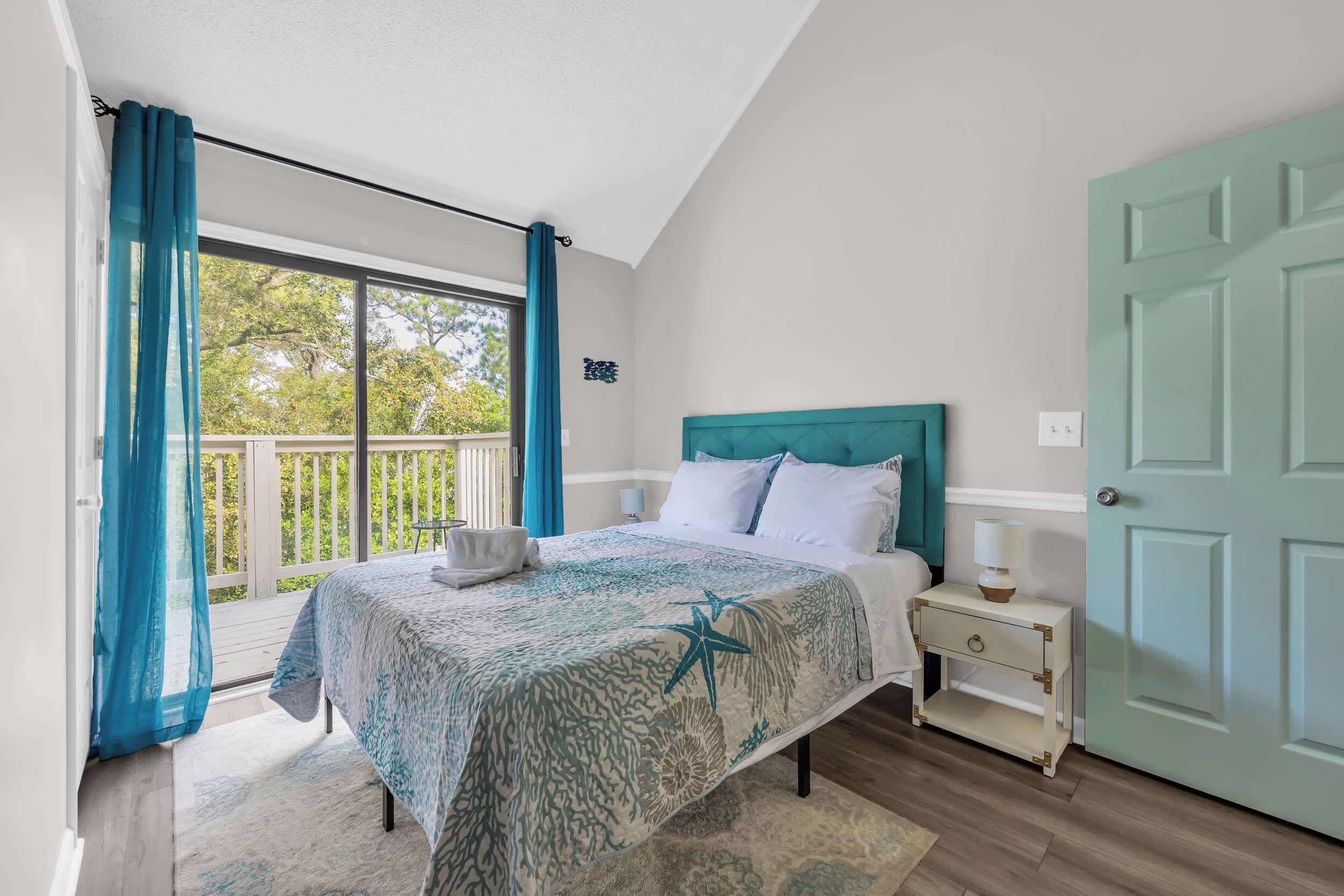 A bedroom with a bed, a nightstand, a door, and a balcony with curtains.