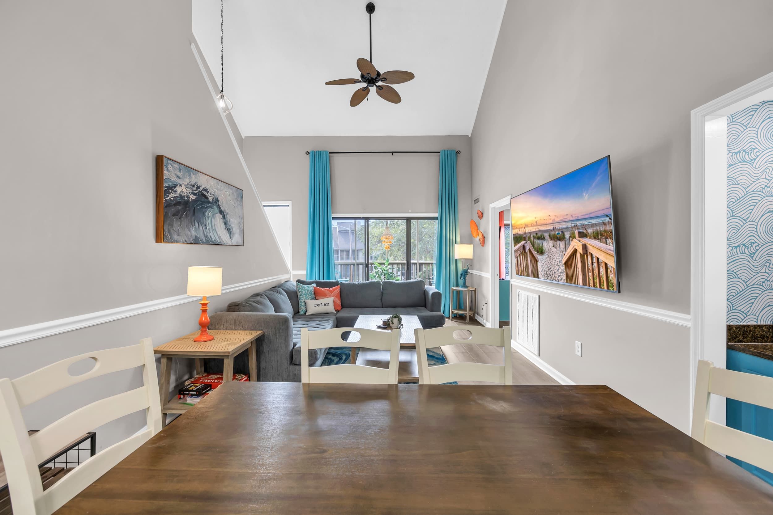 Un salon moderne comprenant un coin repas, un ventilateur de plafond, un canapé, une table basse et une grande fenêtre avec des rideaux.