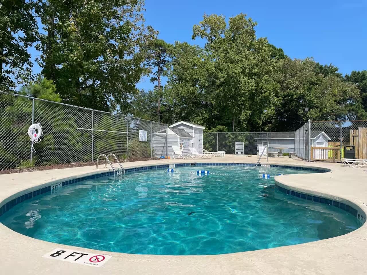 A swimming pool with a diving board, surrounded by a fence and trees.