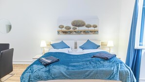 Ein ordentlich eingerichtetes Schlafzimmer mit einem Bett, zwei Nachttischlampen, einem Spiegel und einem an der Wand hängenden Kunstwerk.