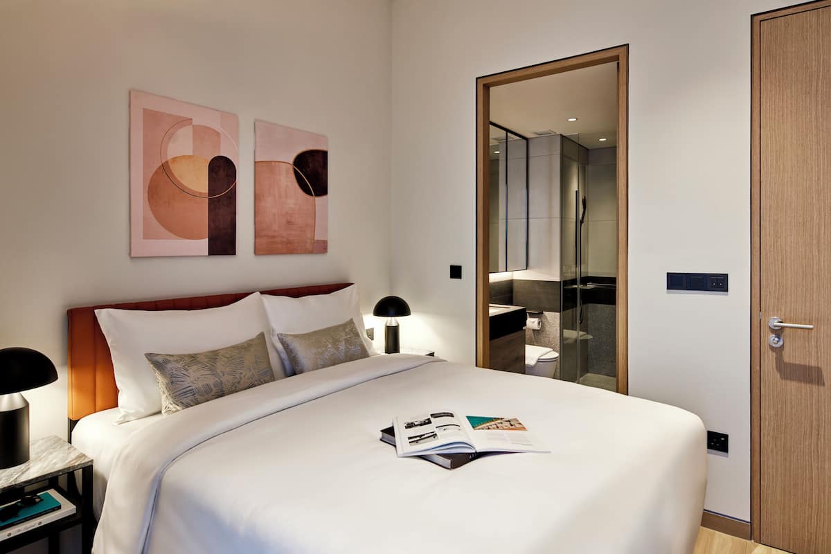 Una habitación de hotel con cama, mesita de noche, espejo y puerta.