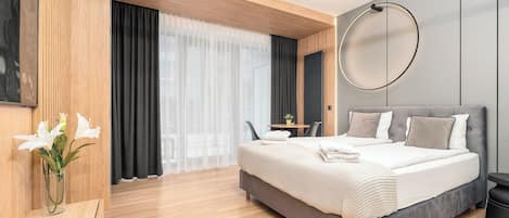 A modern bedroom with a large bed, a bedside table, a chair, a small table, and a large mirror.