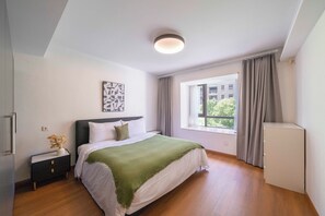 Ein Schlafzimmer mit Bett, Nachttisch, Fenster mit Vorhängen und Deckenleuchte.