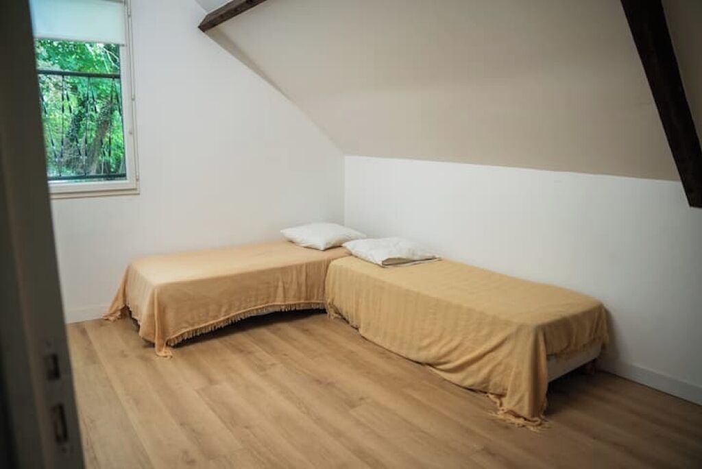 Ein kleines Zimmer mit schrägem Dach, zwei Betten und einem Fenster mit Blick ins Grüne.